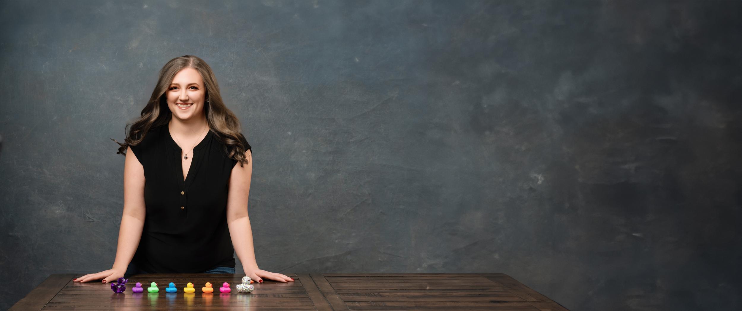 Allie Wickam, a virtual assistant, in a black blouse behind a big wood table with multicolored ducks in a row in front of her