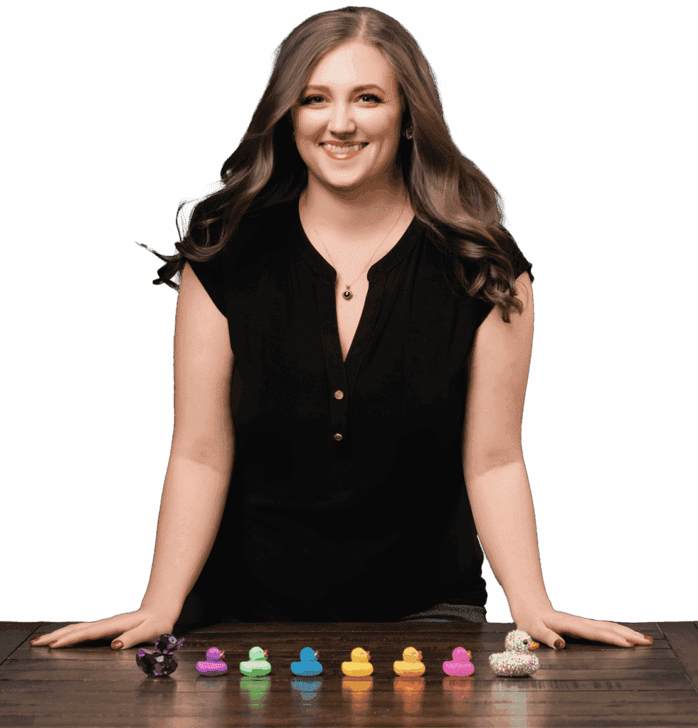 Allie Wickam, a virtual assistant, in a black blouse behind a big wood table with multicolored ducks in a row in front of her