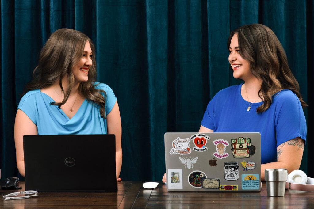 Allie Wickam and her team in blue working on virtual assistant tasks and smiling at each other at a wooden table in front of a dark teal curtain